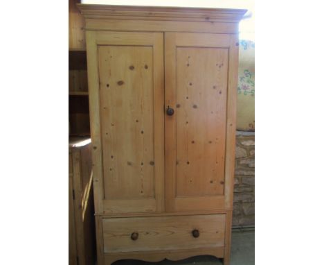 A small stripped pine wardrobe enclosed by a pair of three quarter length panel doors over a long drawer with shaped apron 10