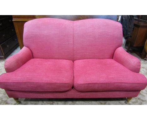 A Laura Ashley 'Howard' style two seat sofa in a cranberry coloured upholstery on turned supports, with brass castors to the 