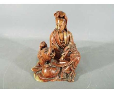 A 19th Chinese soapstone carving depicting Guanyin dressed in flowing robes and holding a scroll, in a seated position next t