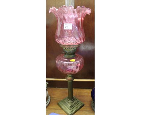 Brass double burner oil lamp with wrythen cranberry glass reservoir on a brass reeded column base, having writhen cranberry g