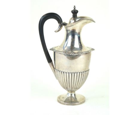 A silver hot water potOf baluster form, with an embossed fluted lower body, an applied gadrooned and foliate rim, ebonised wo
