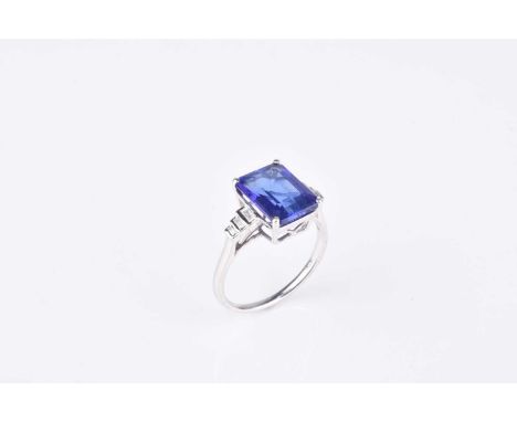 A tanzanite and diamond ring, designed as a central rectangular cut tanzanite claw set in white metal to graduated baguette c