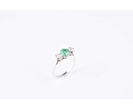 A graduated three stone emerald and diamond ring, designed as a central trap cut emerald flanked to each side by a brilliant 