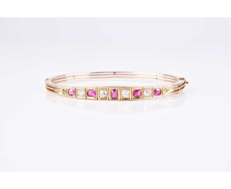 An early 20th century diamond and ruby set hinged bangle, designed as five graduated oval mixed cut rubies interspersed with 