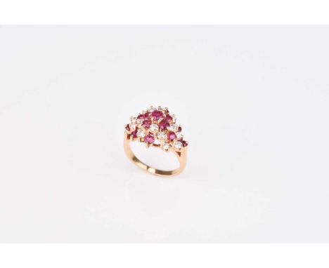 A ruby and diamond cluster ring, designed as a raised cluster of thirteen round mixed cut rubies and fourteen brilliant cut d
