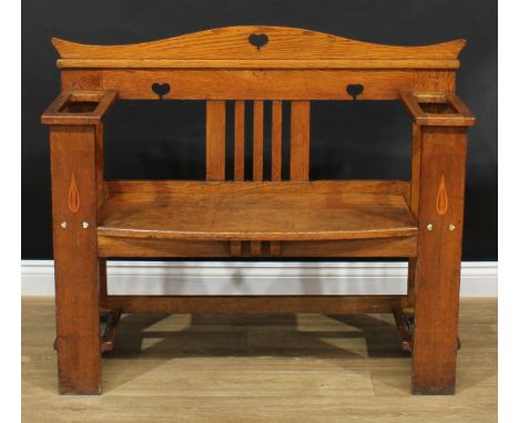 An Arts &amp; Crafts oak hall bench, serpentine crested back pierced with hearts, each arm with a provision for walking stick