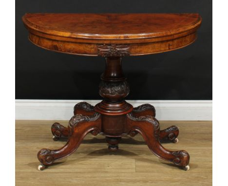 A Victorian walnut demilune card table, hinged top enclosing a baize lined playing surface, turned column carved with leaves,