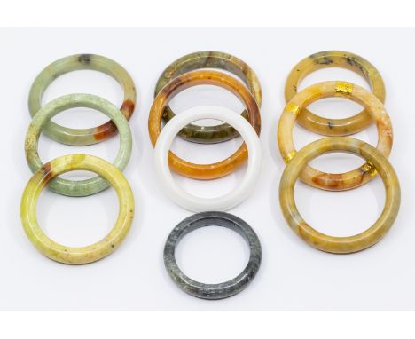 A collection of ten jade/ hardstone bangles in varying shapes and sizes and colours including grey, brown, green, white etc, 