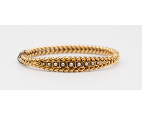 An early 20th century pearl set 15ct gold bangle, comprising a row of graduated half pearls set to the centre, within a rope 