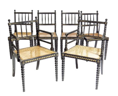 A set of six ebonised dining chairs, with parcel gilt decoration and bobbin turned supports, each with a cane seat and a leop