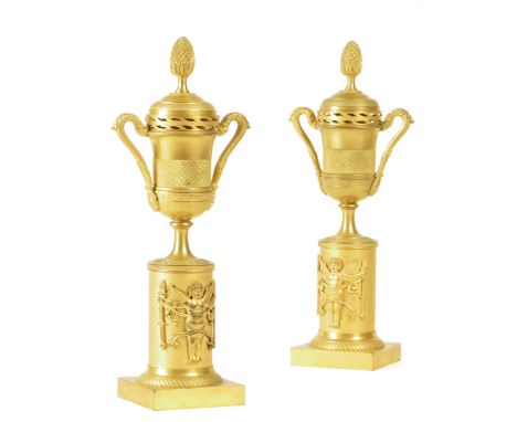 A pair of French Empire ormolu cassolettes, each with a fir cone finial, the reversible top with a candle sconce, above an ur