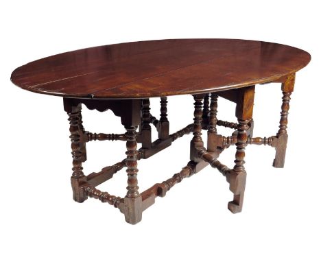 A large 17th century style elm gateleg dining table, the oval drop-leaf top on bobbin and ring turned legs united by peripher
