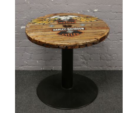 A pub table with metal base, plank top and painted with the Harley Davidson logo.
