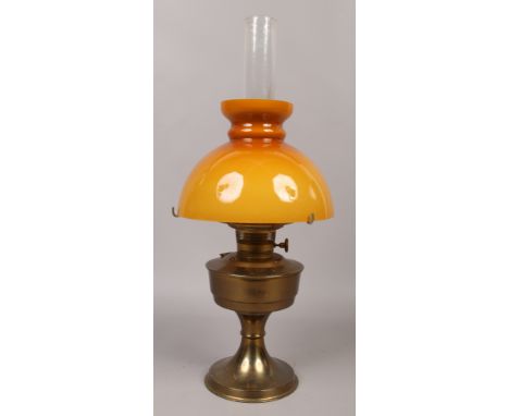 An early 20th century brass based oil lamp with opaque orange glass shade.