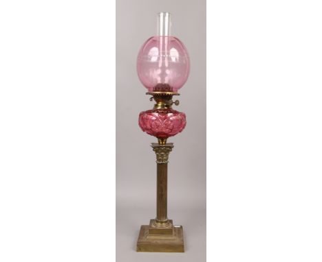 An oil lamp with moulded cranberry glass font and raised on a brass corinthian column base.Condition report intended as a gui