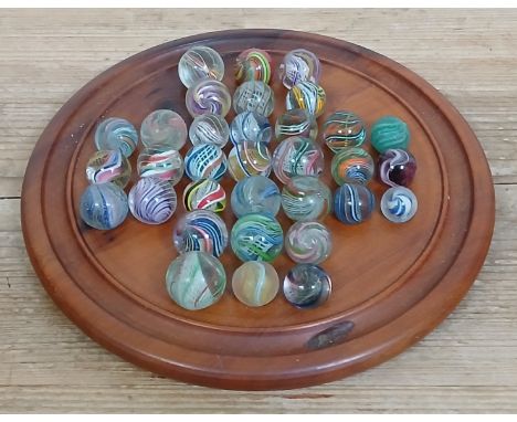 A solitaire board containing 33 hand blown glass marbles including latticino, lobed core swirls etc, ranging in diameter from