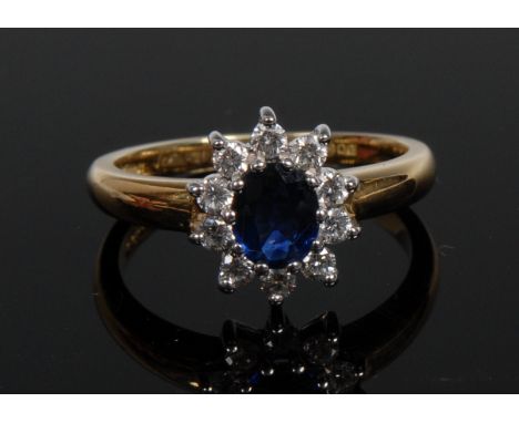 An 18ct gold sapphire and diamond flower head cluster ring, central oval deep blue sapphire surrounded by ten round brilliant