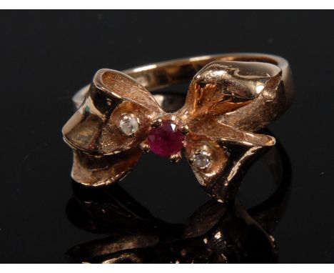 A ruby and diamond ring, tied ribbon bow setting set with a central single round pinky red ruby, flanked by two diamond accen