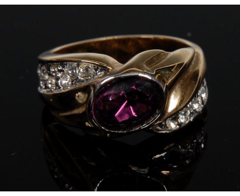 A costume dress ring, central oval paste amethyst effect stone, raised above multi-layer yellow and white metal shoulders set