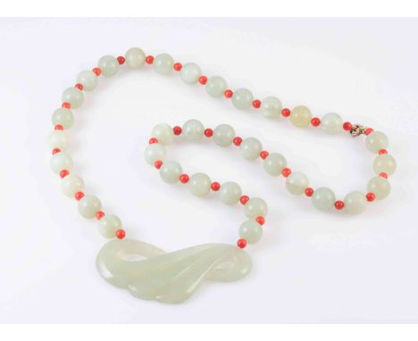 A JADEITE AND CORAL NECKLACE, the carved swirled detail jadeite plaque strung to the bottom of a necklace of thirty four poli