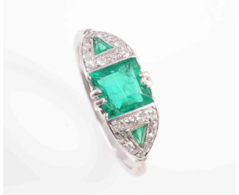 AN ART DECO EMERALD AND DIAMOND RING, the square cut emerald claw and collet set between tapering triangular shaped shoulders