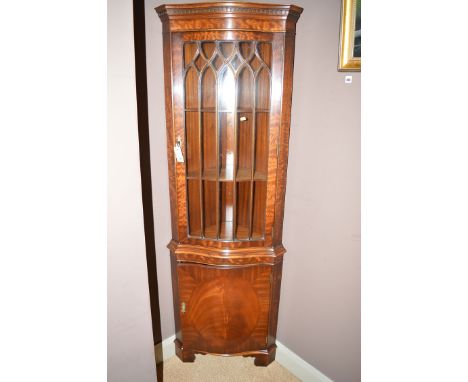 A reproduction mahogany corner cabinet, the flared dentil cornice above arched glazed panel door enclosing shelves, solid ser