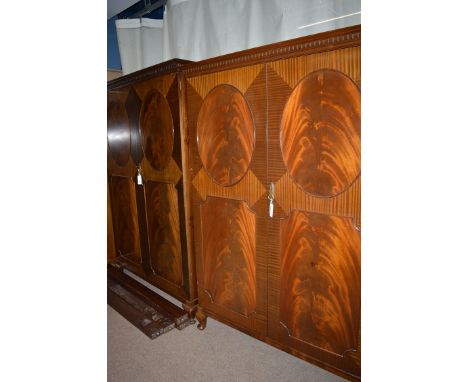 A pair of mid 20th Century mahogany two-door wardrobes, each with flared dentil cornice above oval and canted rectangular pan