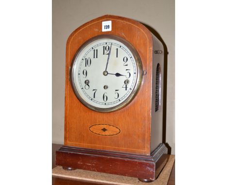 An Edwardian inlaid mahogany mantel clock, the arched case set arabic dial above paterae panel, the plinth base raised on bun