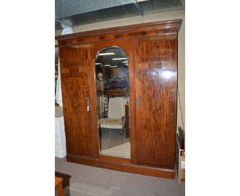 An Edwardian inlaid mahogany three-door wardrobe, the flared dentil cornice above plain frieze, central arched mirror panel d