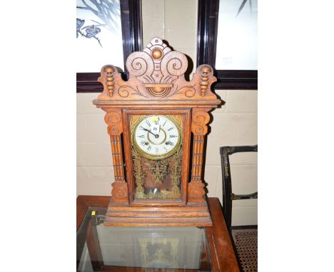 An American style carved oak mantel clock, the pediment with scrolling design, the roman dial enclosed within gilt glass of a