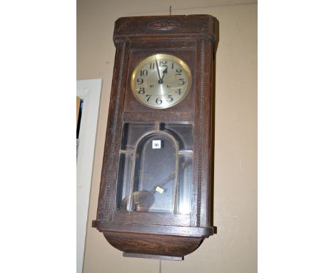 An early 20th Century oak cased wall clock, fitted arabic silvered dial above glazed bevelled panel flanked by beadwork.