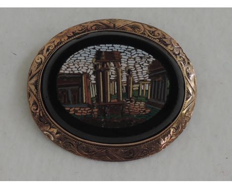 A Grand Tour Italian micro-mosaic brooch depicting Roman ruins inlaid into onyx in a yellow metal surround stamped 9ct
