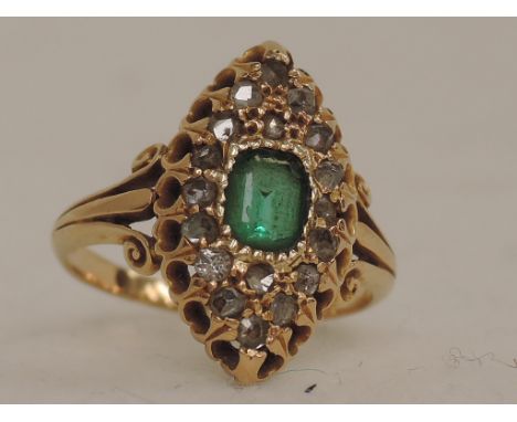 A ladies dress ring having a central baguette cut emerald surrounded by diamond chips in a lozenge shaped mount with moulded 