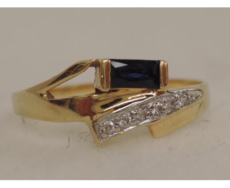 A ladies dress ring of stylised form having a baguette cut sapphire with cubic zirconia decoration on an 18ct gold loop 