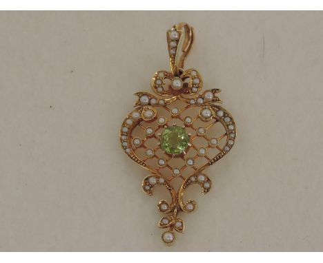 An Edwardian yellow metal pendant stamped 15ct having central peridot with seed pearl bow and trellis decoration with further