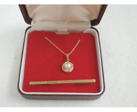 A simulated pearl pendant on a 9ct gold chain and a yellow metal tie bar stamped 9ct having engine turned decoration