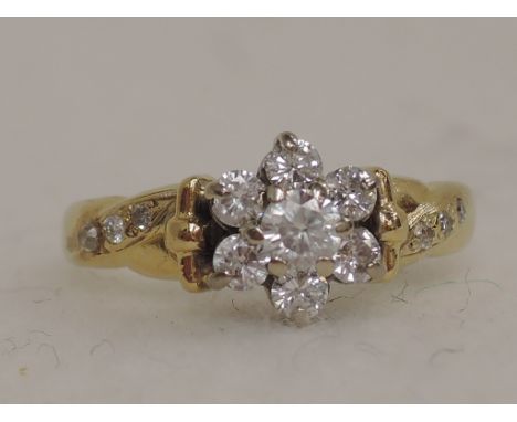 A ladies dress ring having a diamond daisy cluster with further chips to shoulders on an 18ct gold loop