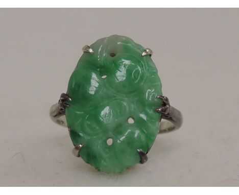A ladies dress ring having an oval carved and pierced jade panel in a claw mount on a white metal loop, no marks