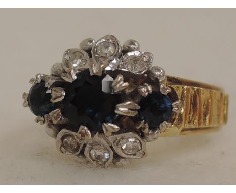 A ladies dress ring having three graduated sapphires with diamond decoration in a stylised mount on a bark effect 18ct gold l