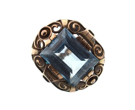 Synthetic spinel yellow metal dress ring, the rectangular blue stone within an openwork scroll border, unmarked, size T appro