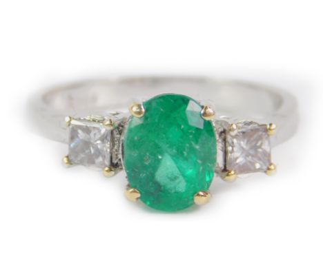 An emerald and diamond three stone ring, set in white metal stamped 18ct, the oval cut emerald approx 1.8ct, princess cut dia