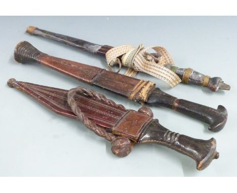 Three African/Asian tribal daggers each with leather scabbard and shaped handle, longest 36cm