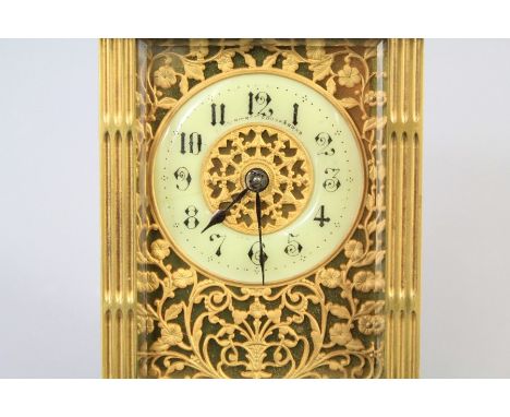 An Edwardian Ornate Brass Carriage Clock. The clock with reeded columns and handle, embossed gilt banded panels and corner fi