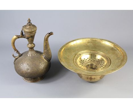 An Islamic Brass Ewer and Basin. The ewer of ovoid design on spreading foot with hinged cover, the body profusely engraved wi