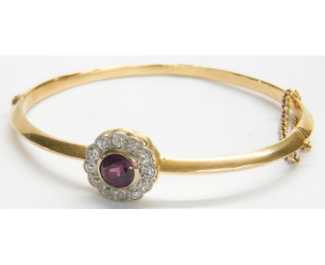 Garnet and diamond yellow gold bangle, with a circular cluster of round-cut diamonds with a central garnet with safety chain,