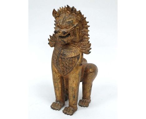 A Chinese Gilt Metal Model of a Temple Lion, wearing an elaborate head-dress and chest plate in a standing pose, 28.5cm high.