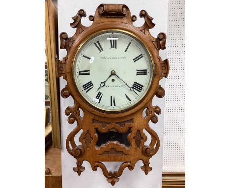 An Early XX Century Hanging Drop End Wall Clock, the oak case carved with scrollwork, the circular white enamel dial with bla