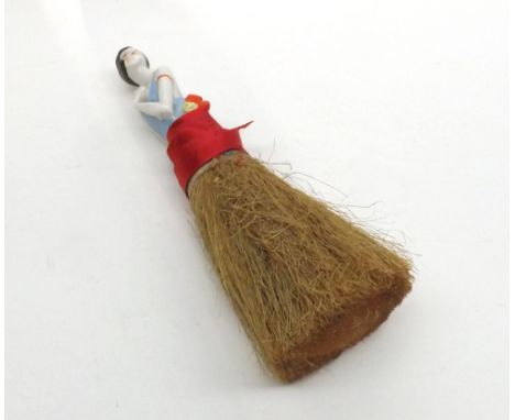 An early 20th Century Novelty Brush, with ceramic handle, modelled as an Art Deco dressed lady, 9” long