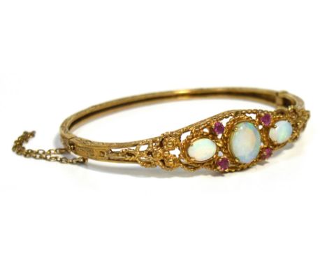 A yellow metal bangle with engraving to either side, the centre filigree set with one large oval opal and two smaller either 