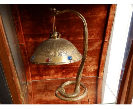 An early 20thC brass table lamp in the form of a coiled snake with a domed shade suspended from its mouth, the shade set with